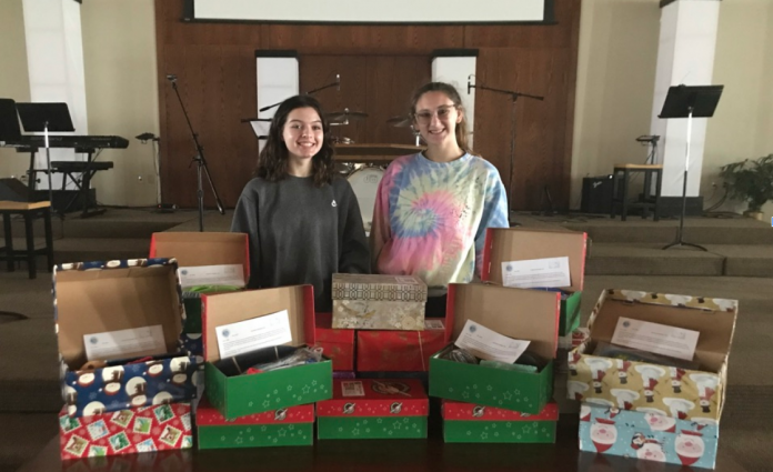Two women standing behind festive shoe boxes, filled with various items.